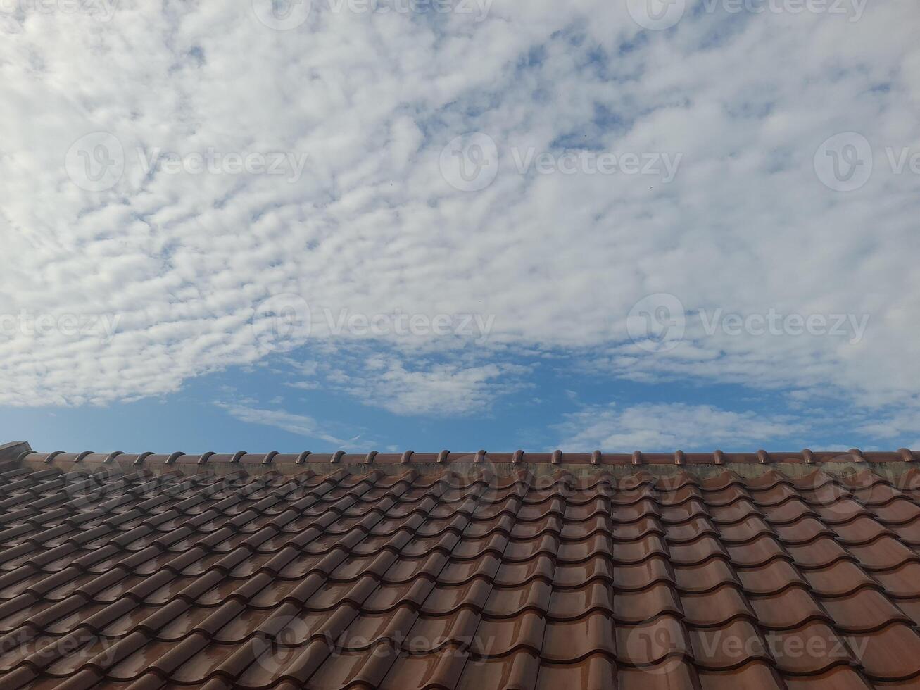 A tiled rooftop under a sky filled with scattered clouds and patches of blue. The scene captures a peaceful, sunny day with a blend of architectural and natural elements. photo