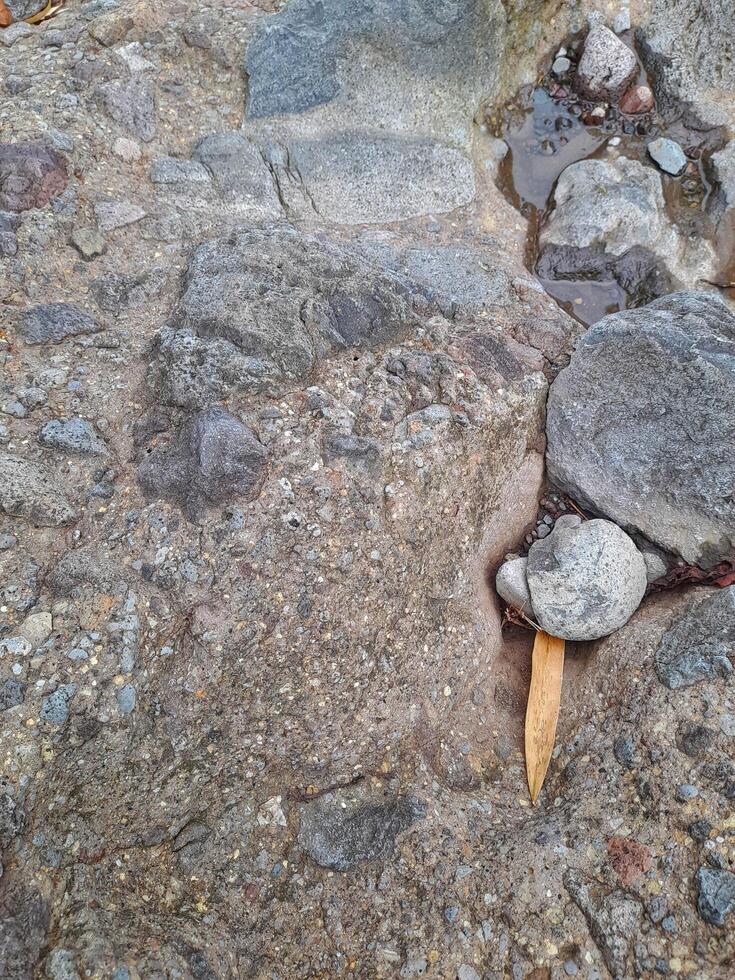 Close up of a natural rock surface with a rough, uneven texture, visible cracks, and earthy tones, showing signs of weathering and mineral deposits. photo