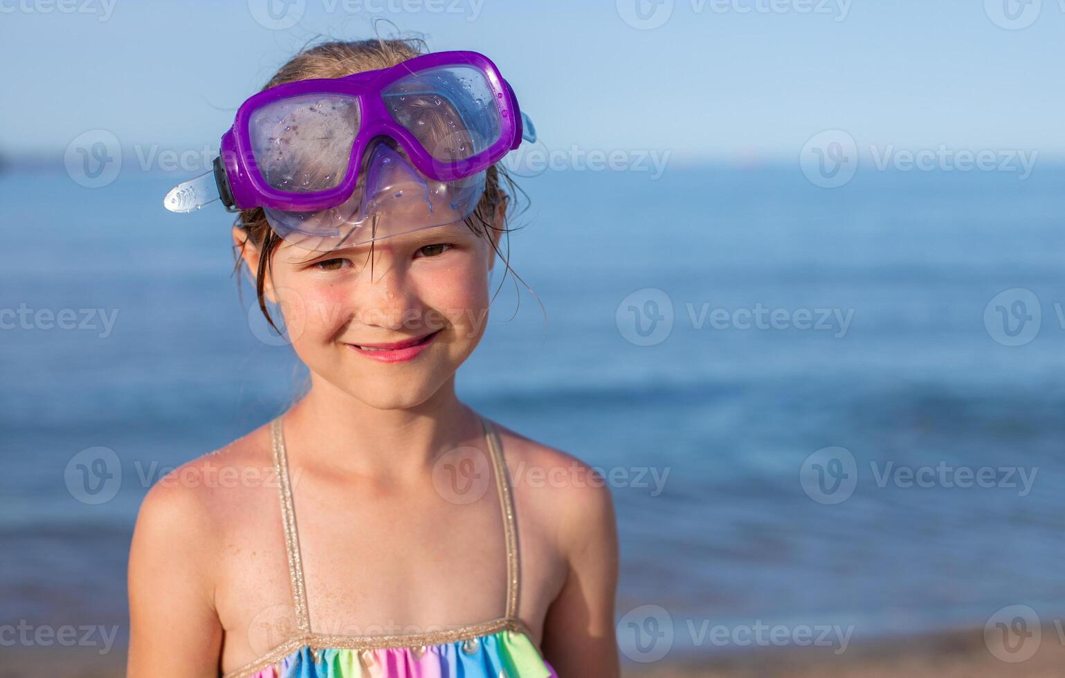 Toddler girl with purple snorkeling goggles smiling on beach. photo