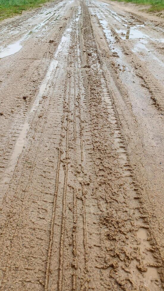 A dirty country narrow road. After the rain, puddles, mud and tire marks formed on the road. Shot on a phone photo
