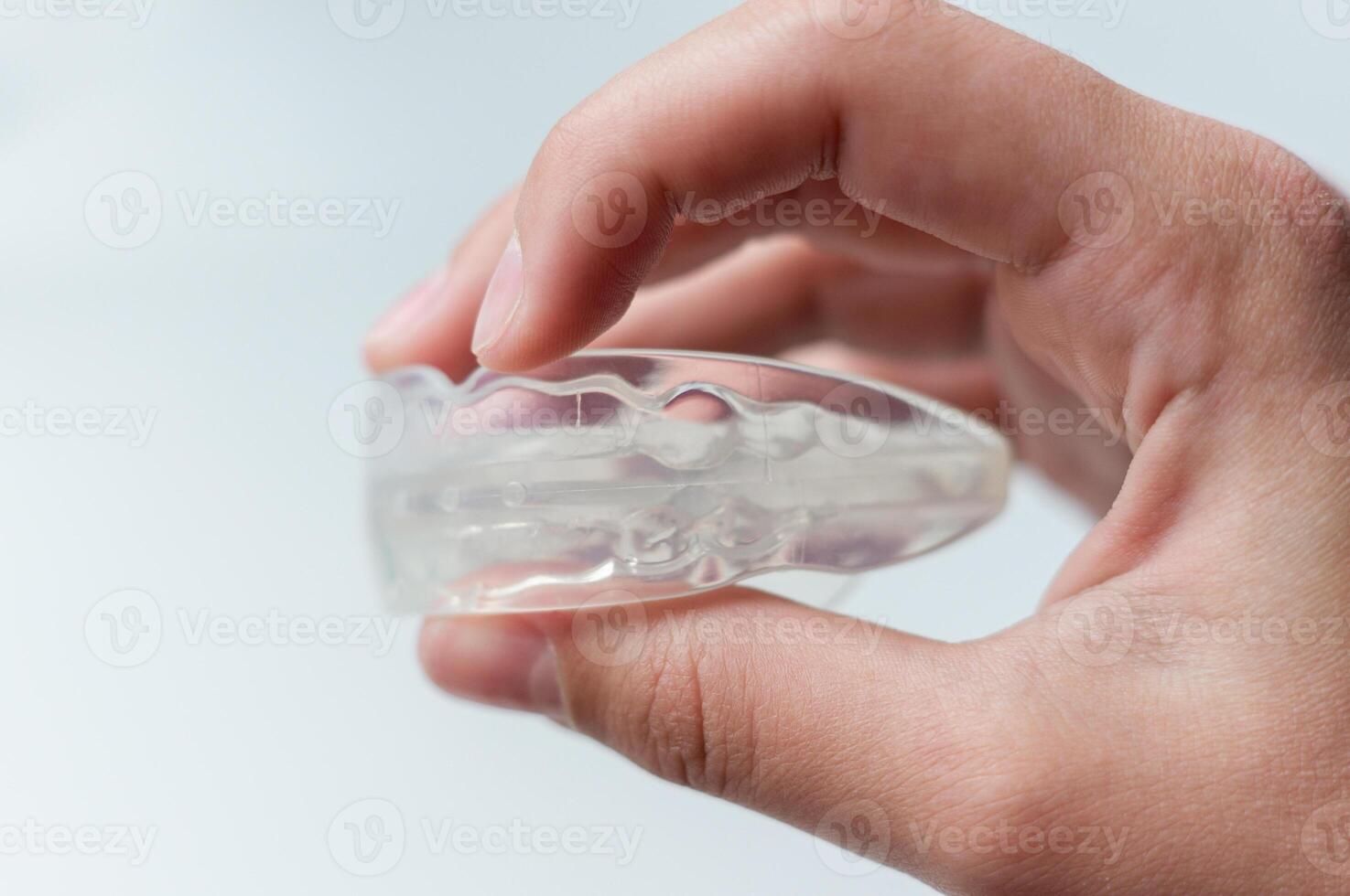 Person holding orthodontic silicone mouth guard for straightening or whitening children's teeth. Side view, close-up, on white background photo