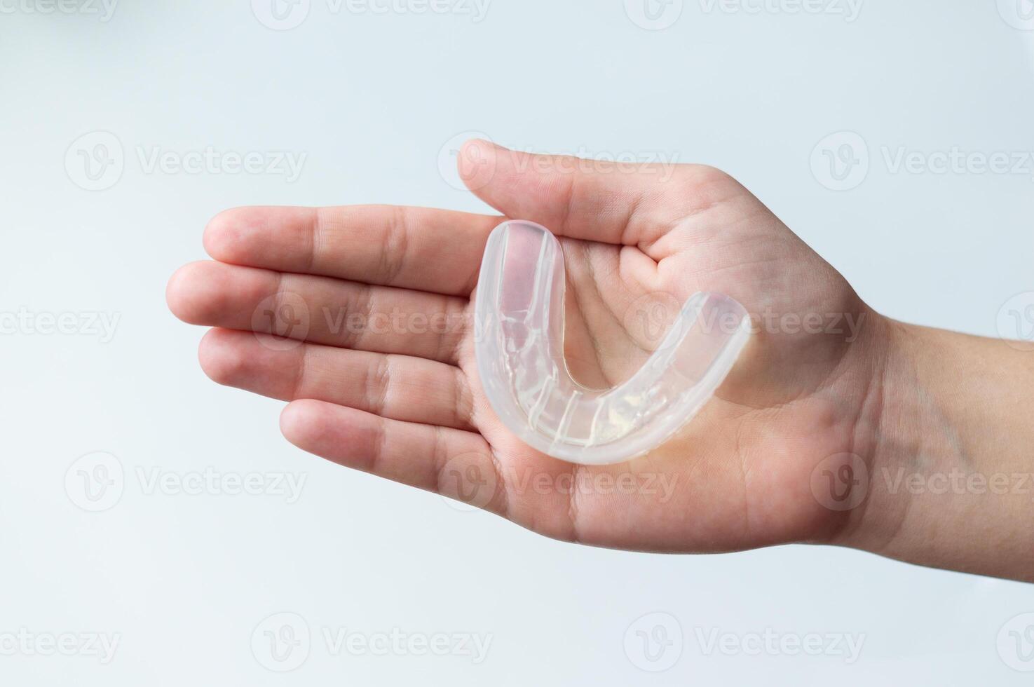 A mouth guard for bite alignment or teeth whitening lies on a person's palm. Top view, close-up, on a white background photo