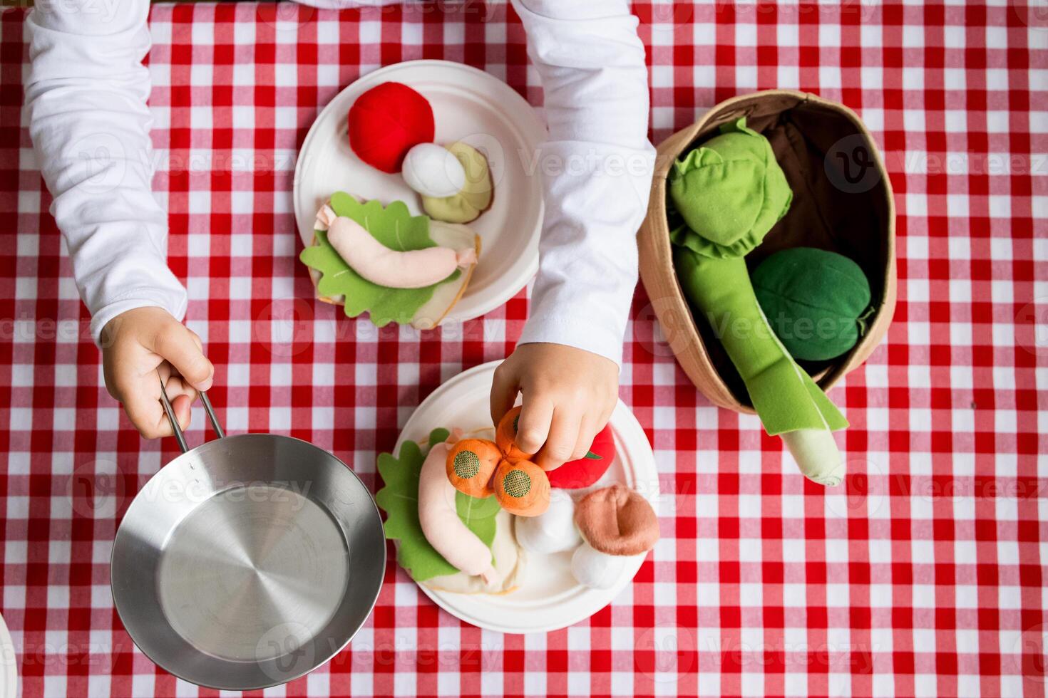 Child playing with colorful felt vegetables on red checkered tablecloth photo