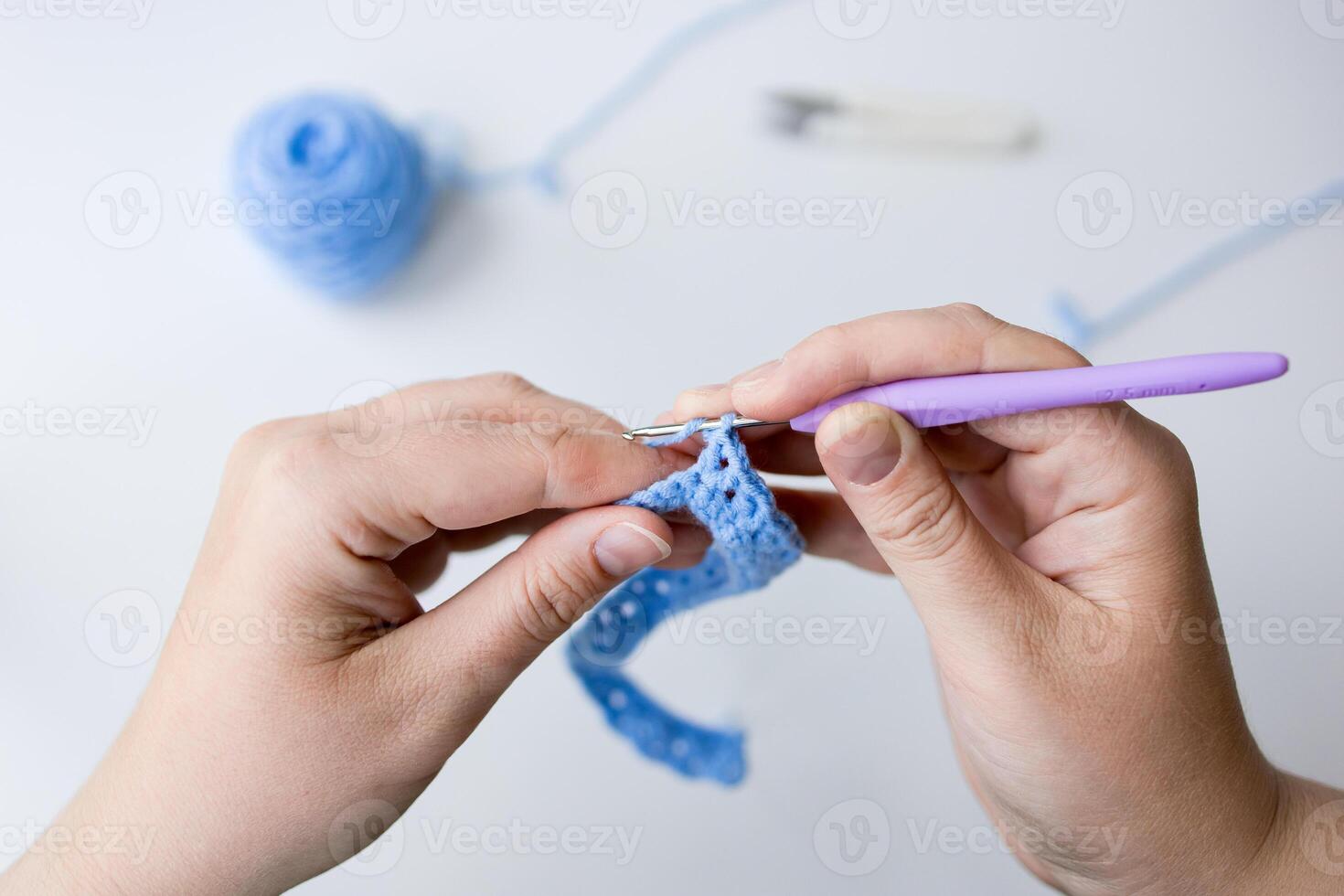 Close up of crocheting hands with purple hook and blue yarn photo