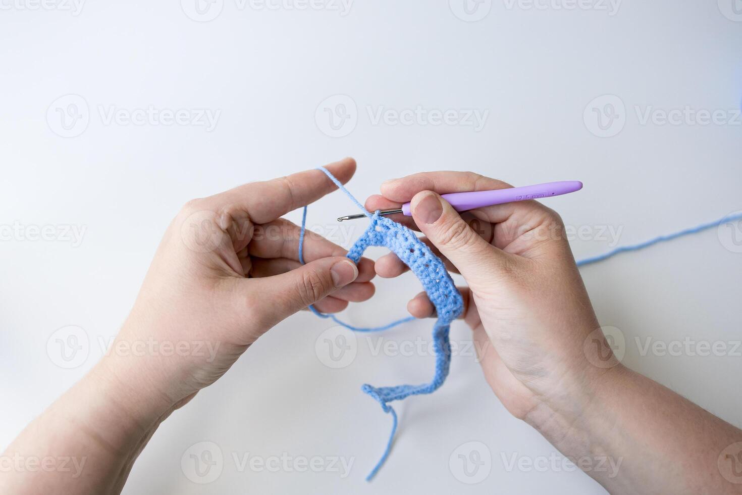 Hands crocheting with blue yarn using purple hook photo