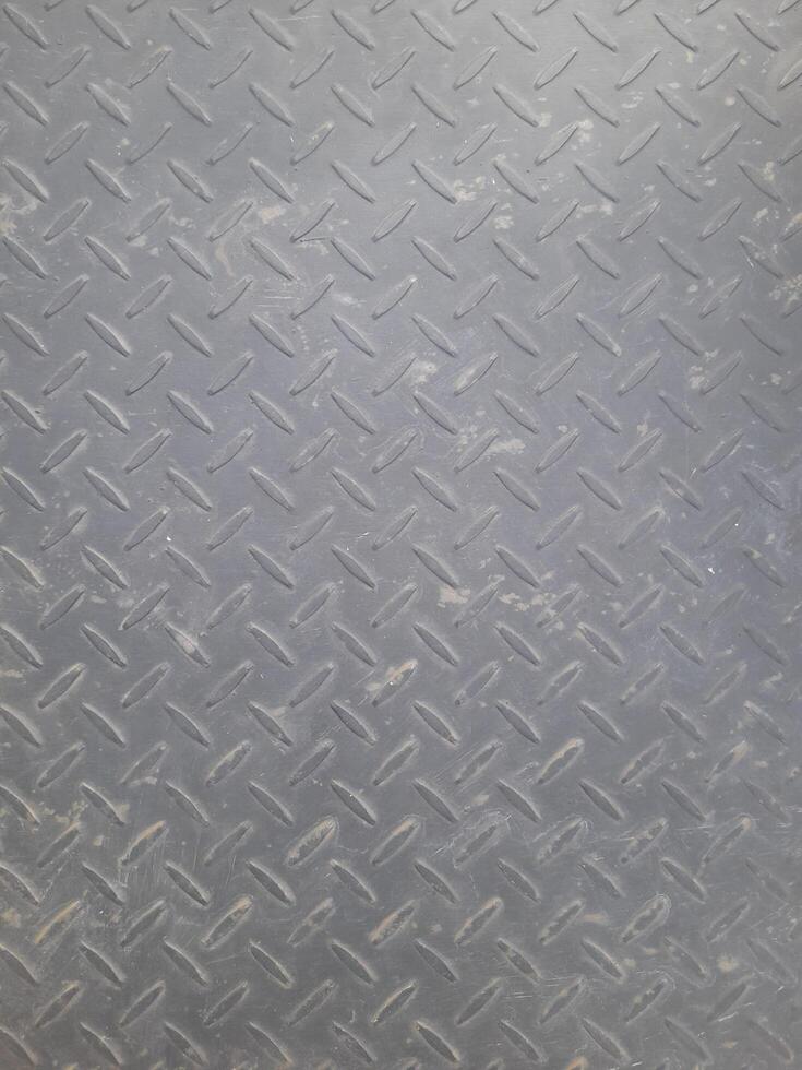 Close-up of a gray metal diamond plate surface with visible wear, scratches, and a repeating raised pattern for grip. photo