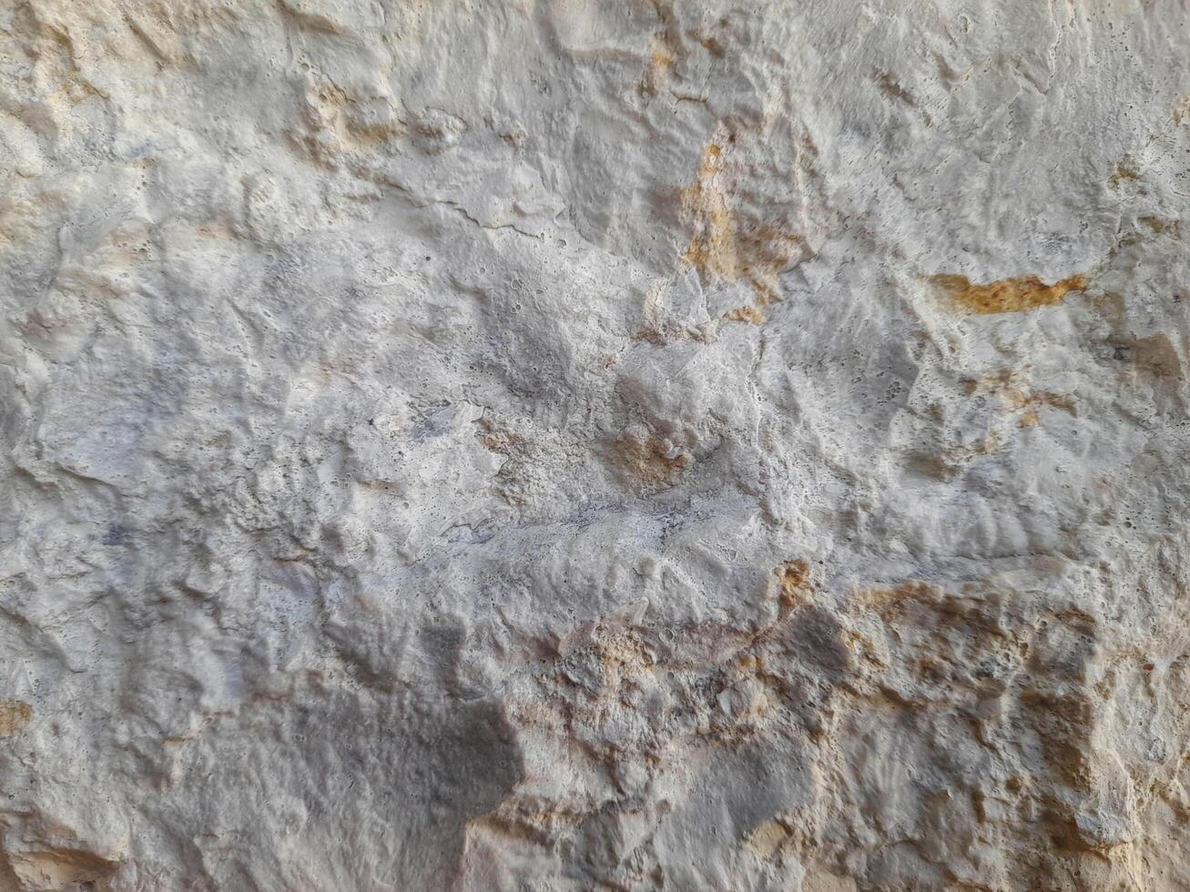 Rough stone surface with mixed beige and gray tones, showing natural erosion, uneven texture, and layered mineral patterns photo