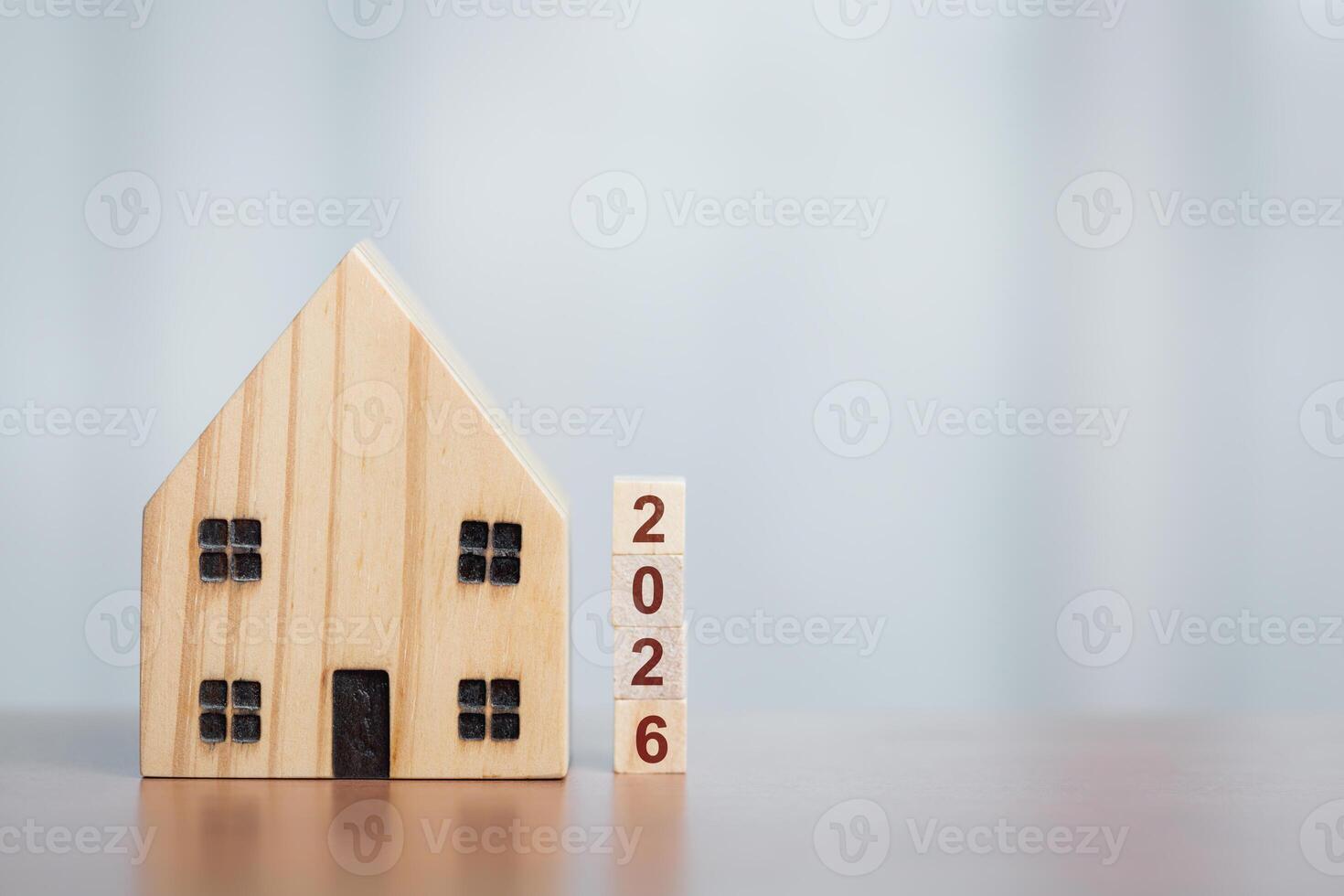 A wooden house model sits beside stacked blocks forming the year 2026, symbolizing future housing plans or real estate aspirations. photo