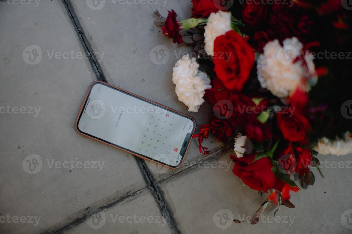a smartphone is lying on the ground next to a bouquet of red flowers photo