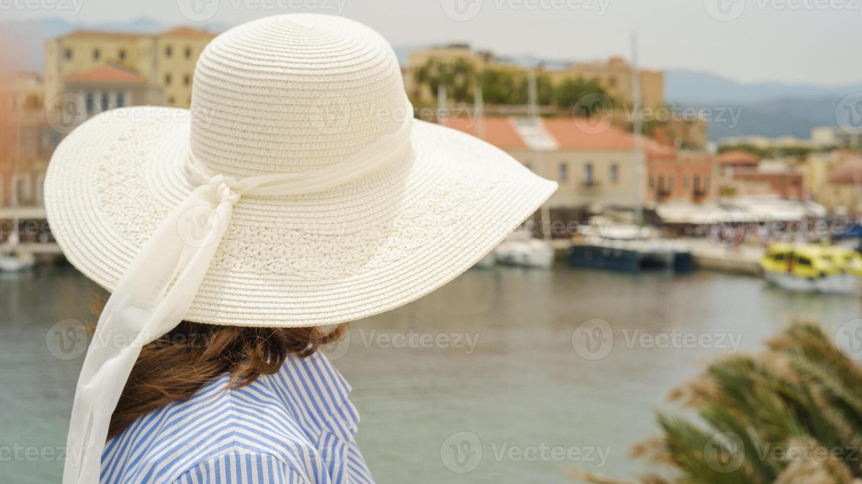 Tourist wearing white sun hat looking at chania venetian harbour in crete, greece photo