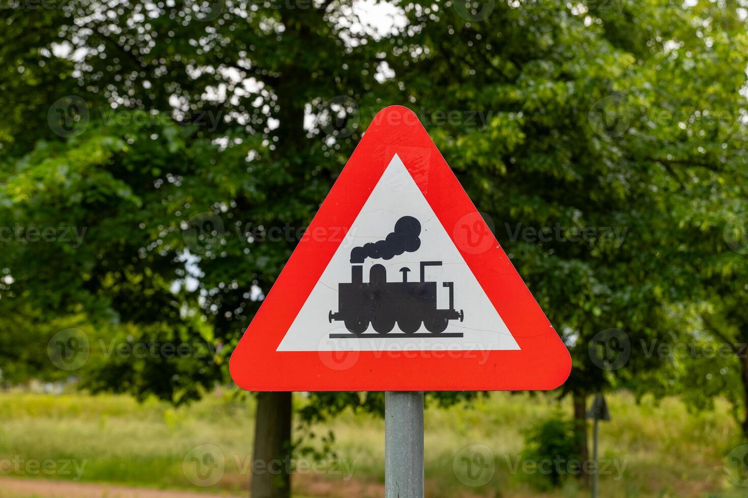 Train warning sign stands alert amidst lush greenery on a sunny day in the countryside photo