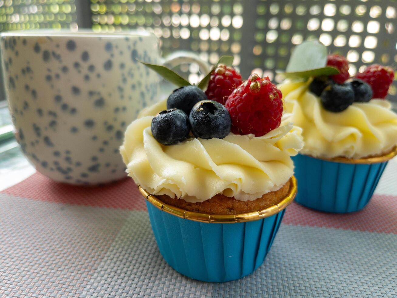 Cupcake with Berries and Coffee Mug on Outdoor Table. Delicious cupcake with cream frosting, blueberries, raspberries photo