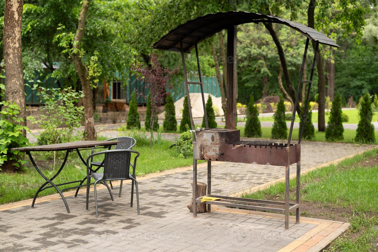 Outdoor barbecue grill with canopy, metal table, and chairs in a green garden setting, perfect for summer picnics and gatherings. photo
