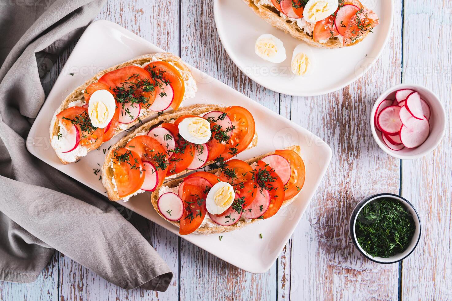 Appetizing bruschetta with ricotta, tomato, radish and quail egg on a plate top view photo