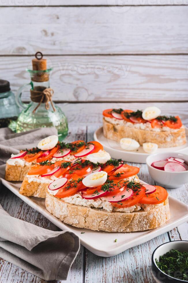 Appetizing bruschetta with ricotta, tomato, radish and quail egg on a plate vertical view photo