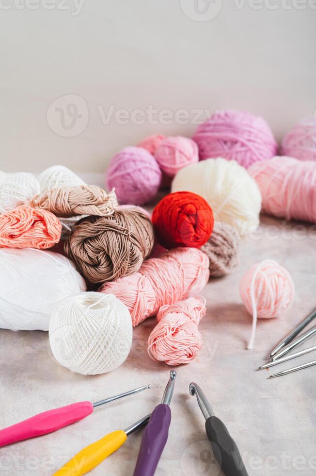 Lots of colorful skeins of yarn, crochet hooks and knitting needles on a table vertical view photo