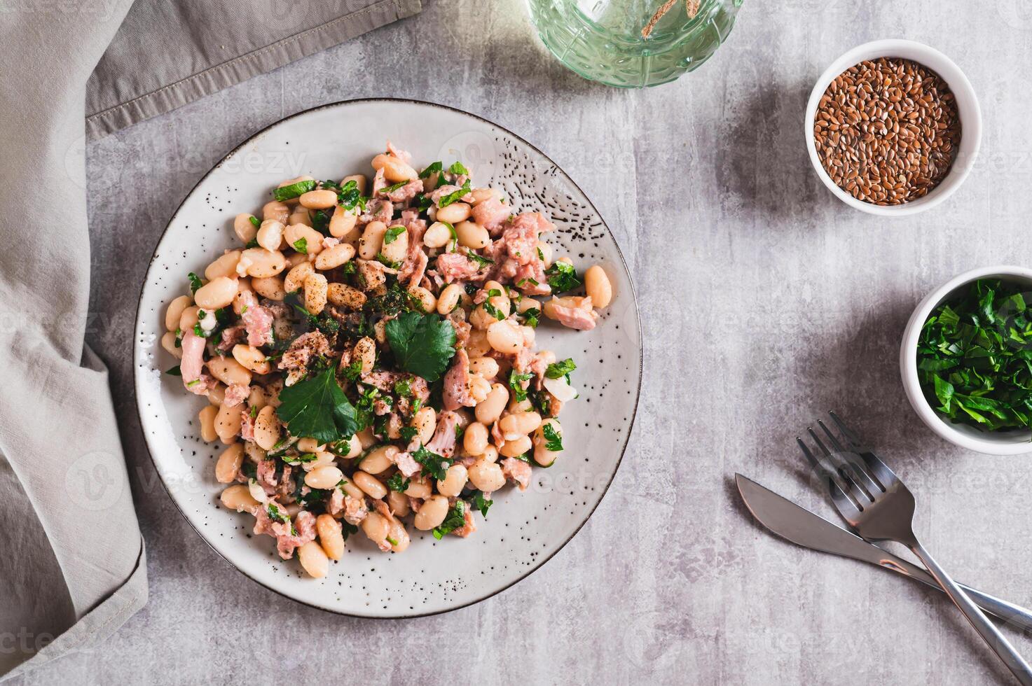 Appetizing salad with tuna, white beans and greens on a plate on the table top view photo