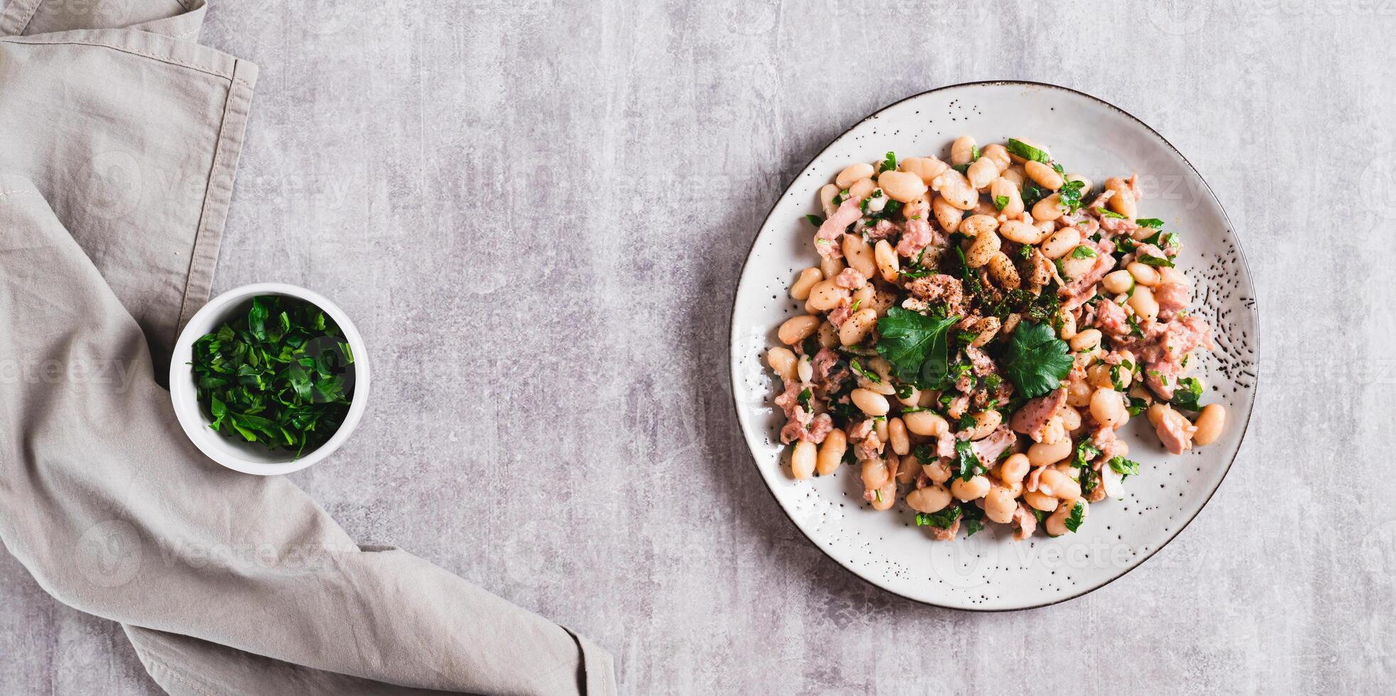 Protein tuna, beans, herb salad on a plate on the table top view web banner photo