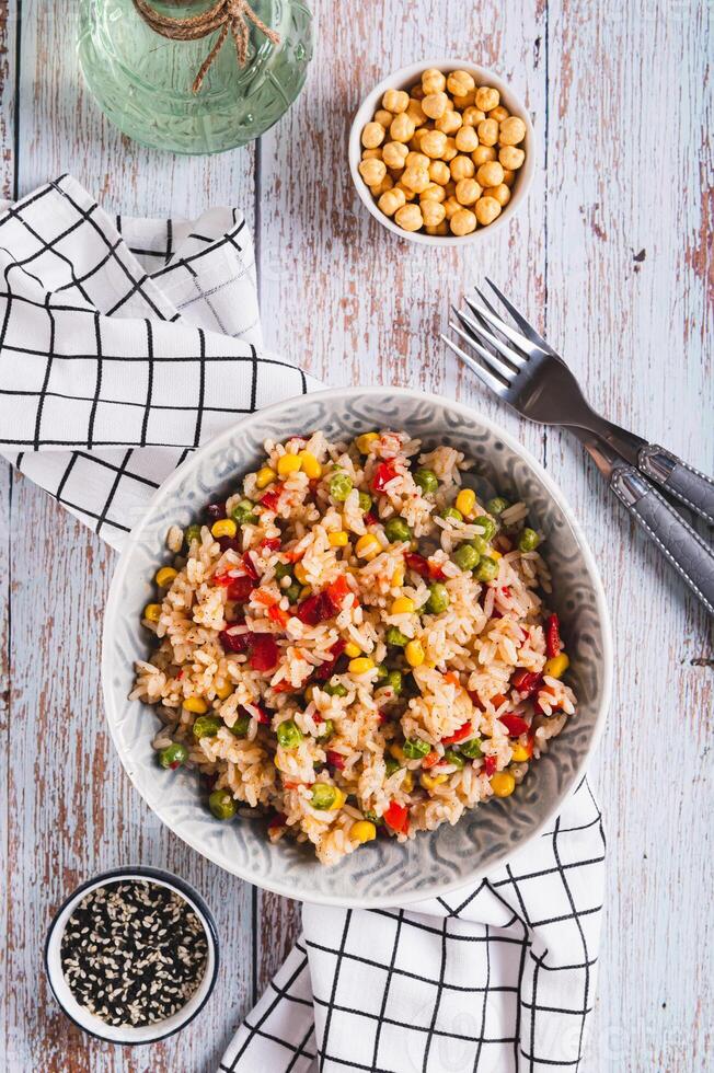 A bowl of cooked rice and vegetables for garnish on the table top and vertical view photo