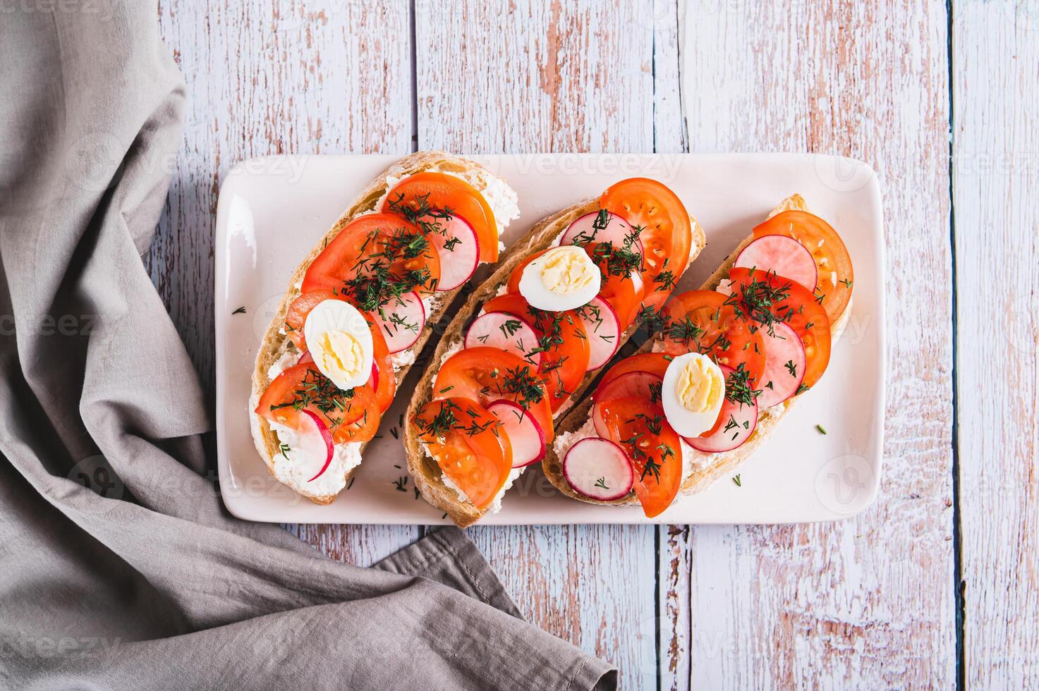 Close up of bruschetta with ricotta, tomato, radish and quail egg on a plate top view photo