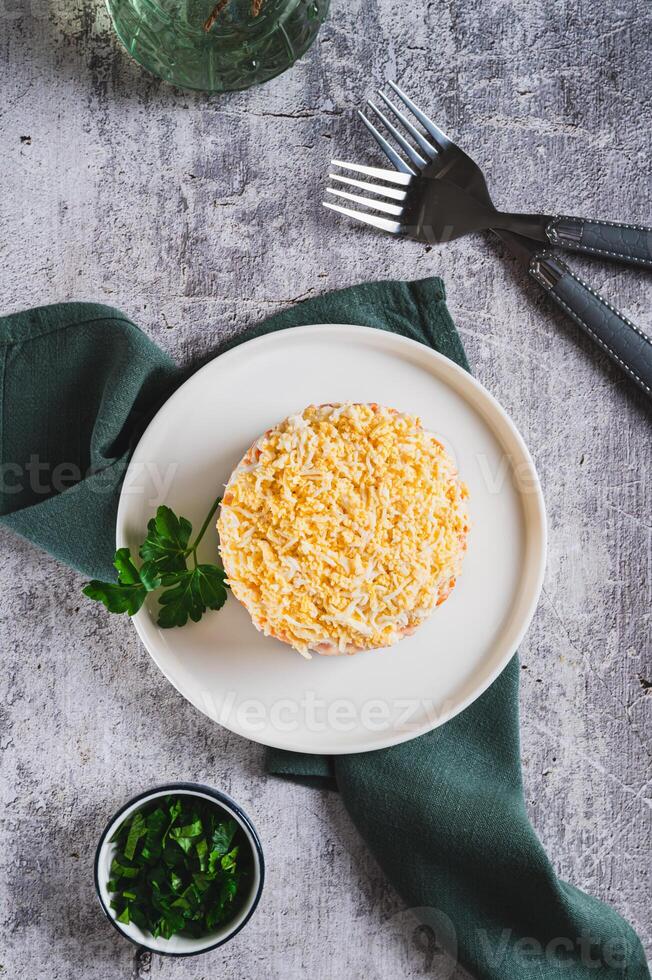 Classic mimosa salad with canned fish and vegetables on a plate on the table top and vertical view photo