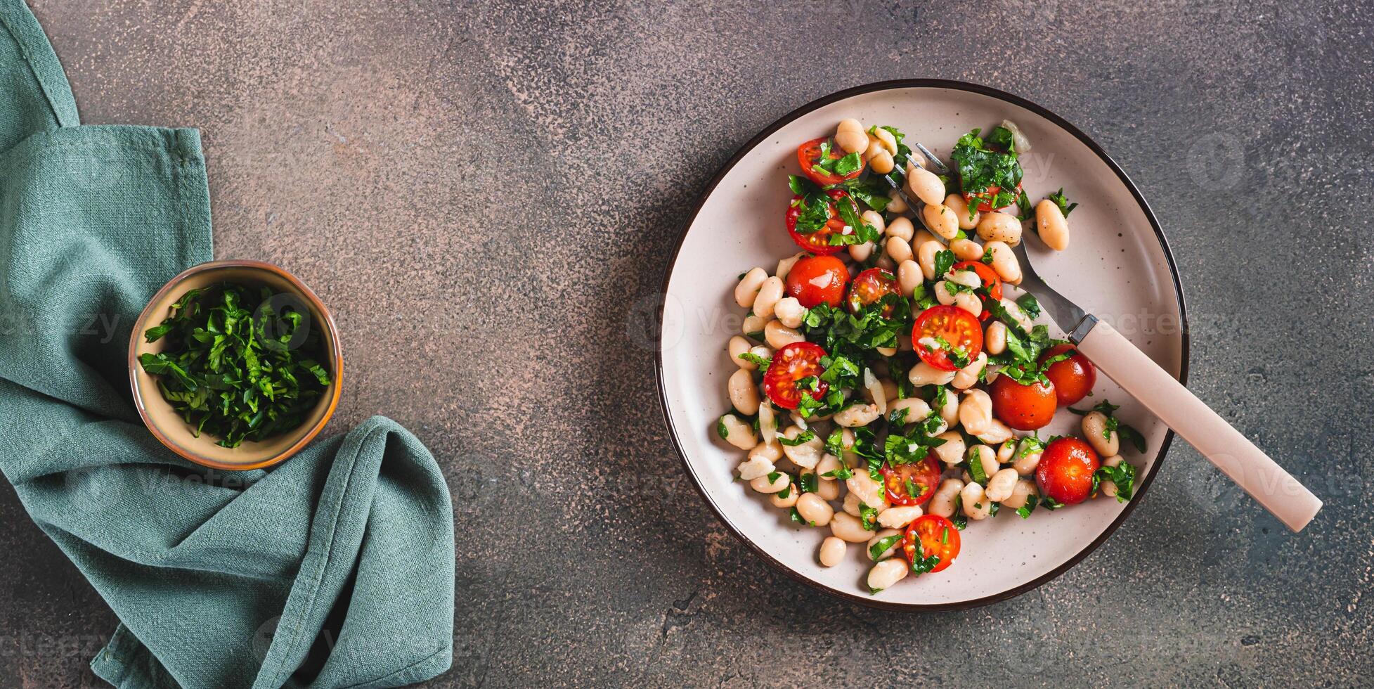 Vegetarian white bean, tomato and herb salad on a plate on the table top view web banner photo