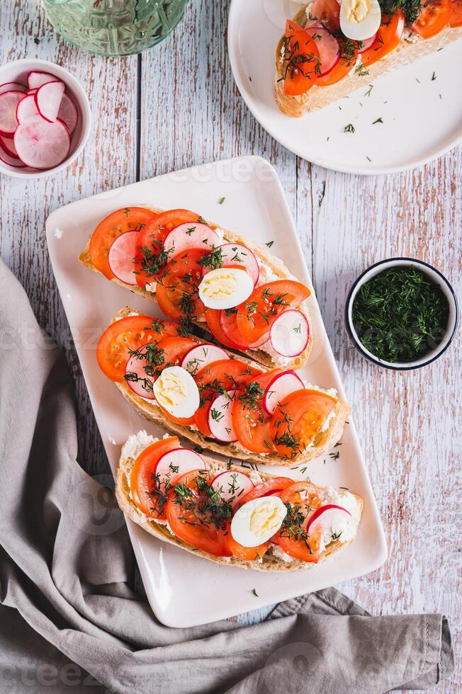Sandwiches with ricotta, tomato, radish and egg on a plate on a table top and vertical view photo