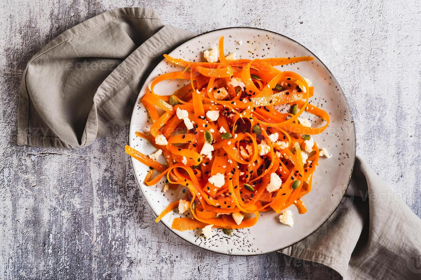 Close up of spicy carrot, ricotta and pumpkin seed salad on a plate on a table top view photo