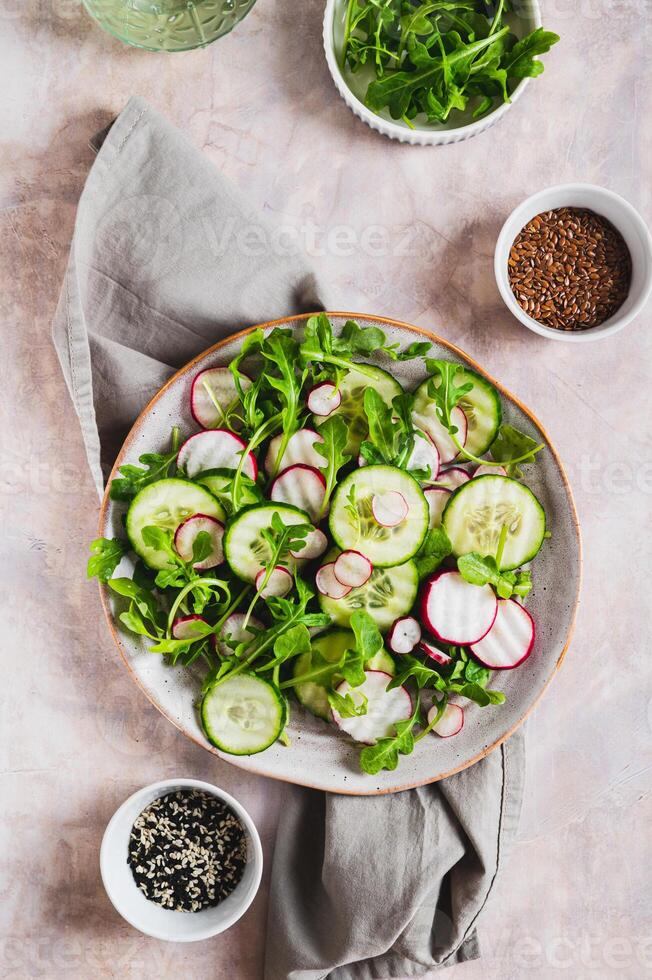 Cucumber, radish and greens salad mix on a plate on the table top and vertical view photo