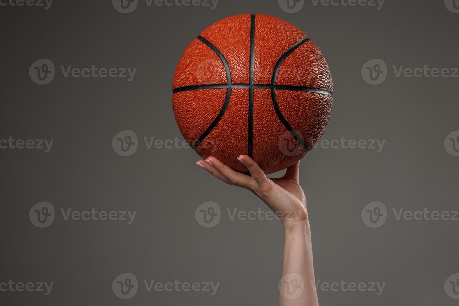 Close up of a woman hand confidently holding a basketball high against a dark background, symbolizing strength, sports, and empowerment in a minimalist composition. photo
