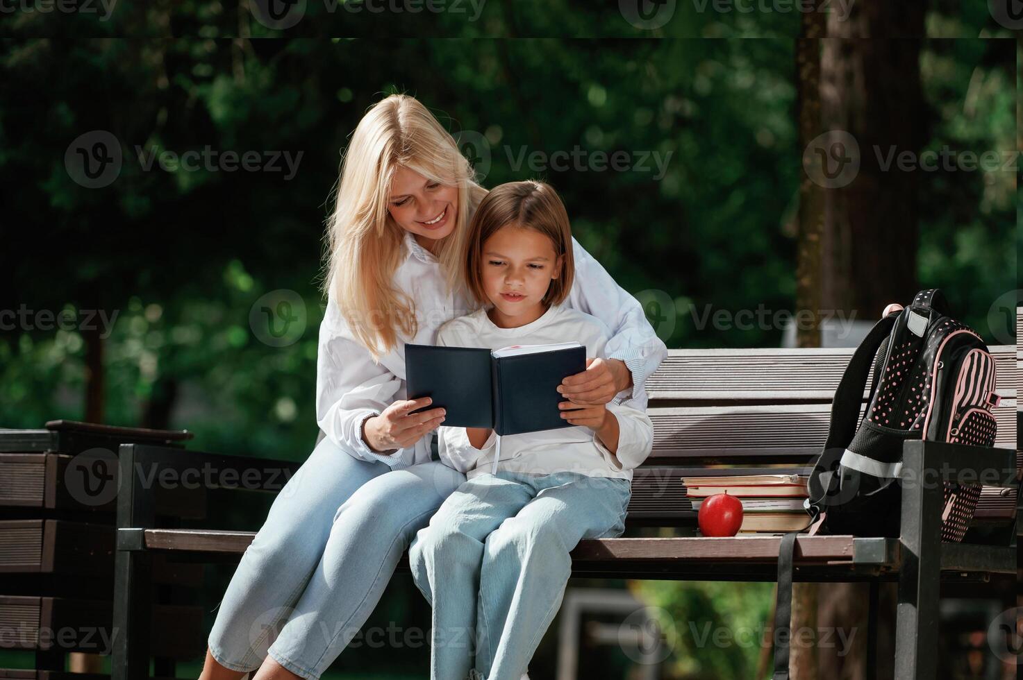 Information in notepad, ,,,,reading it. Little schoolgirl with her mother are sitting on the bench outdoors photo