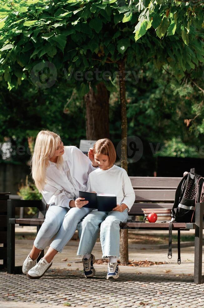 Information, in notepad, reading it. Little schoolgirl with her mother are sitting on the bench outdoors photo