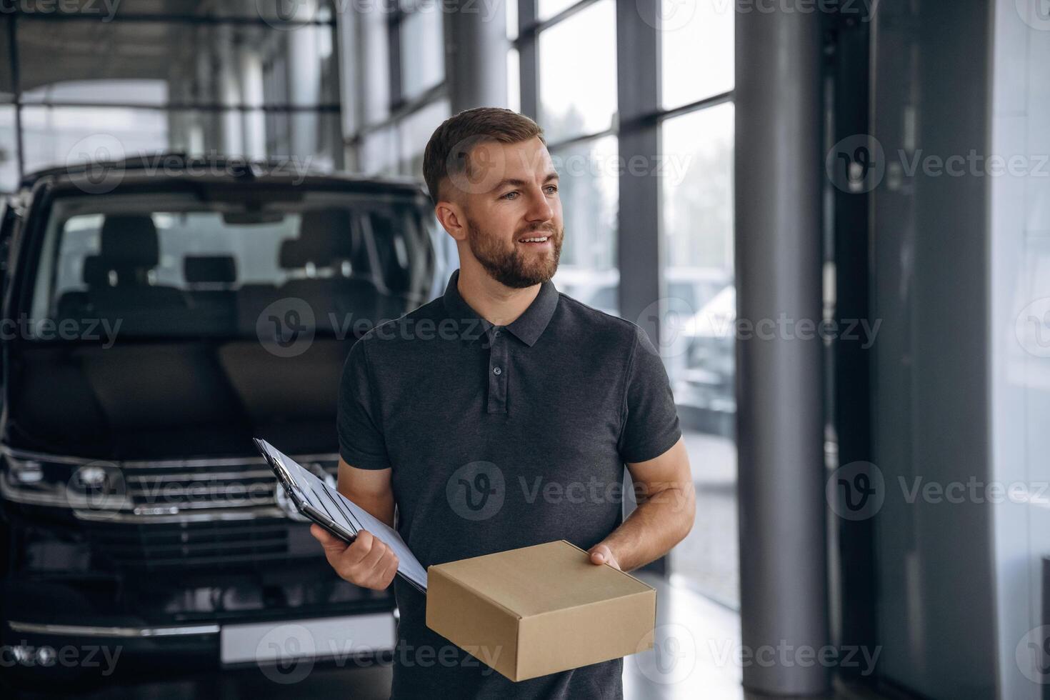 Standing, holding notepad,,. Delivery man or loader is near the car with a box photo