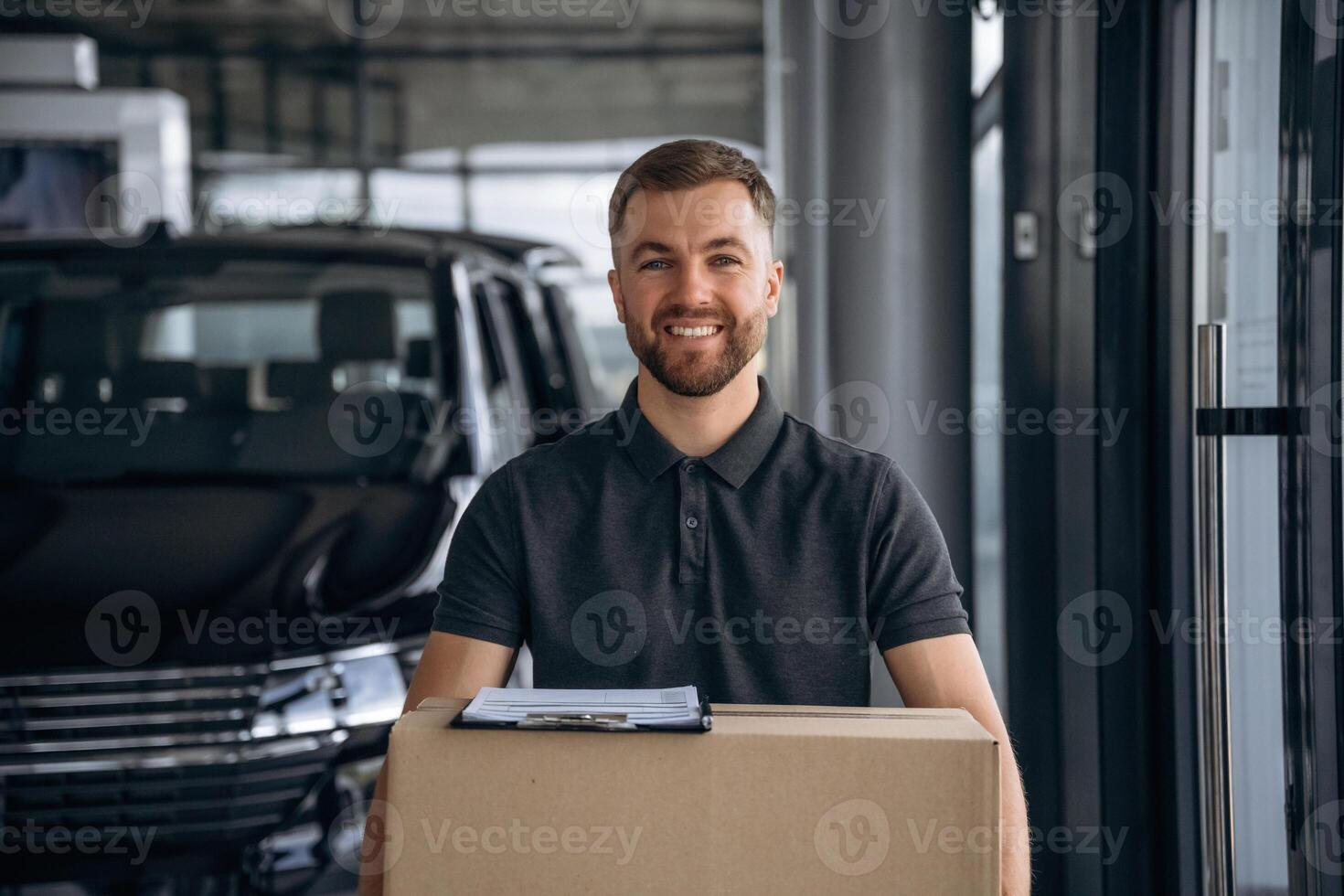 Smiling, positive facial ,,expression. Delivery man or loader is near the car with a box photo