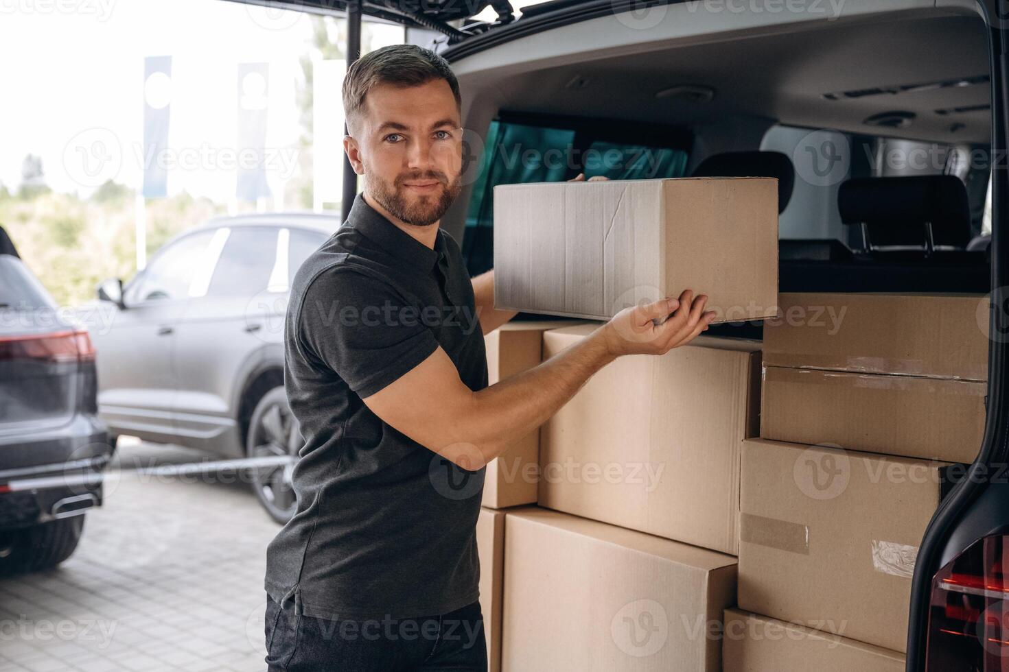 Holding ,the, packed product in hands. Delivery man or loader is near the car with a box photo