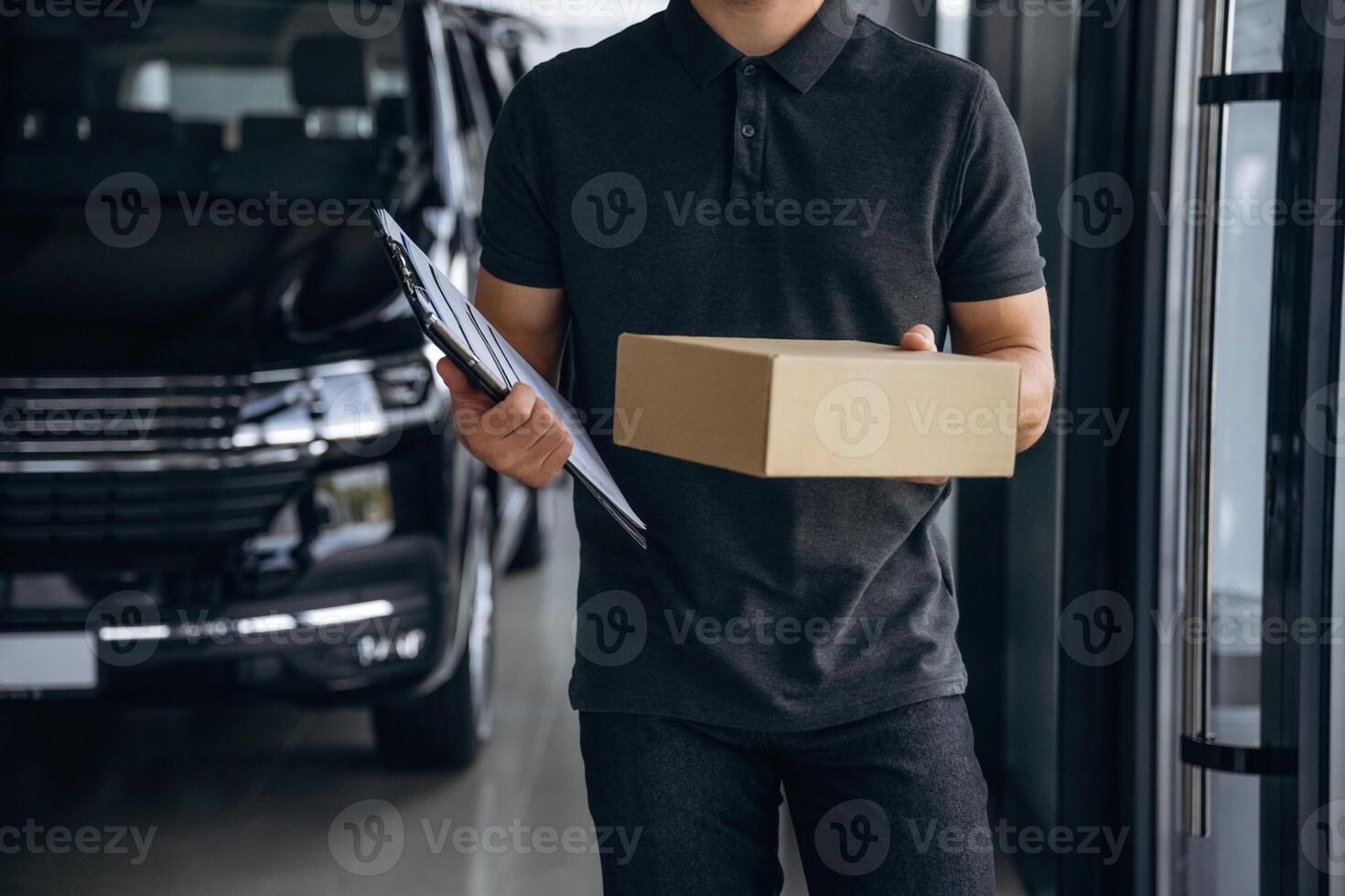 Front view, standing., Delivery, man ,or loader is near the car with a box photo