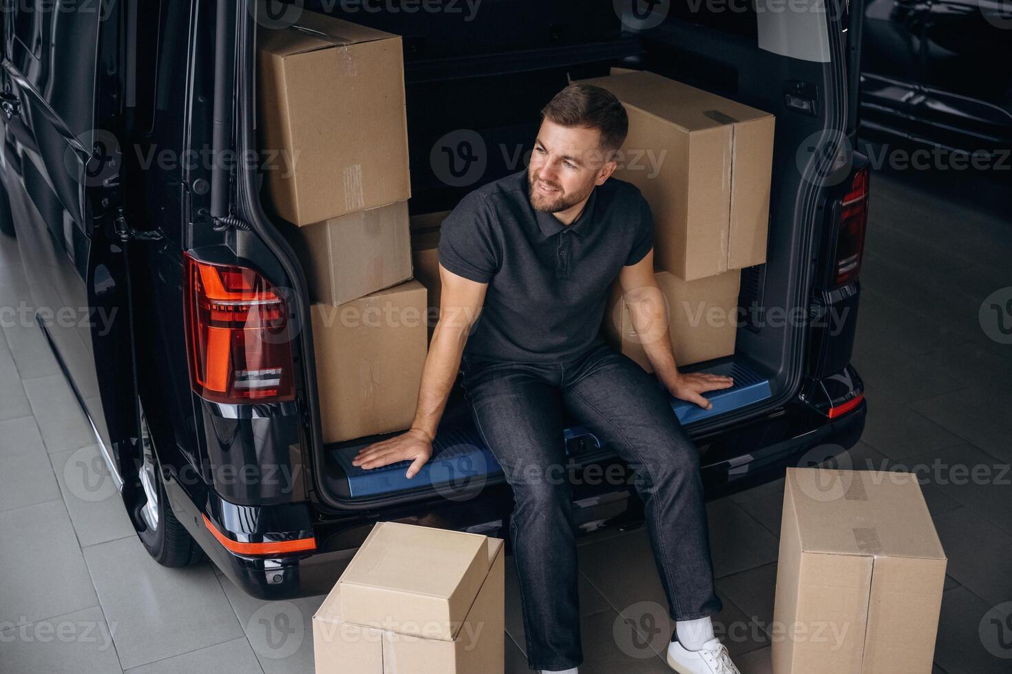 Taking a break,, resting, sitting. Delivery man or loader is near the car with a box photo