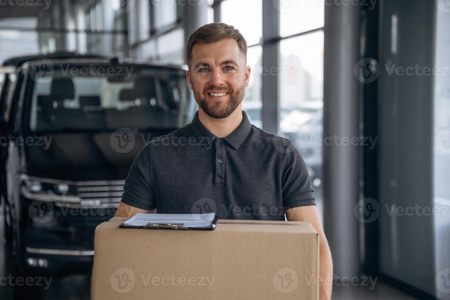 Smiling, ,positive facial, expression. Delivery man or loader is near the car with a box photo