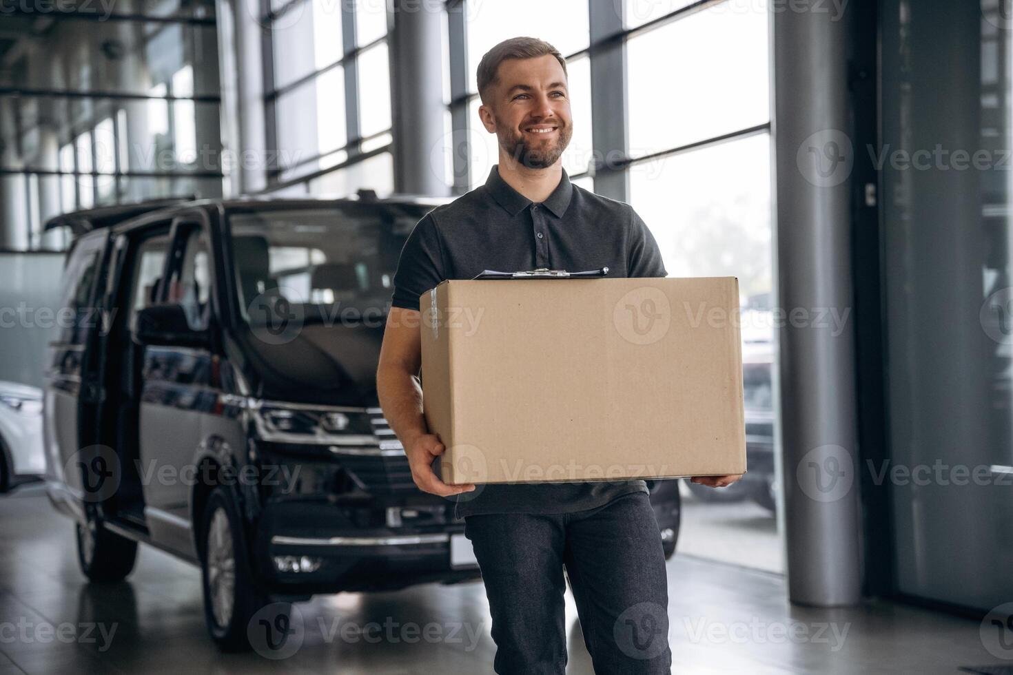 With ,a ,box, smiling. Delivery man or loader is near the car photo