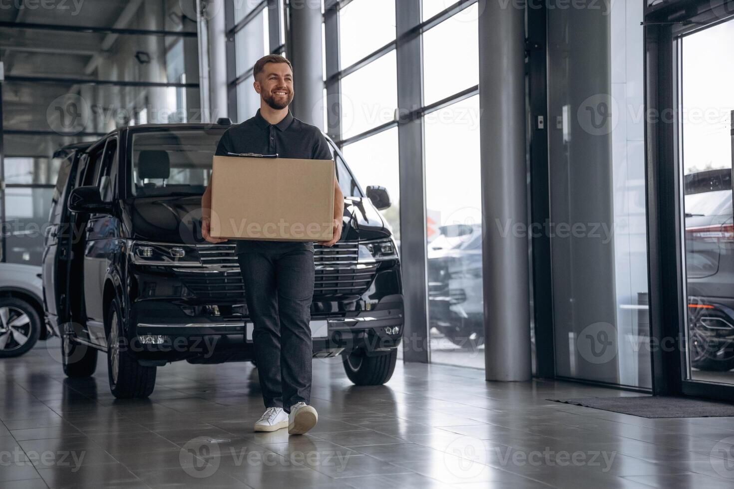 Smiling,, positive facial expression. Delivery man or loader is near the car with a box photo