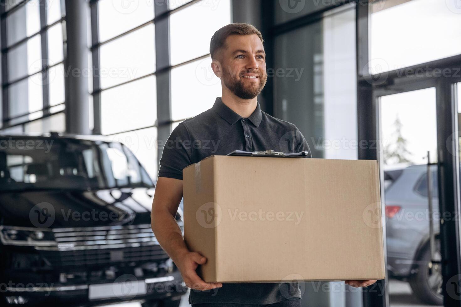 With a, box, smiling. Delivery man or loader is near the car photo