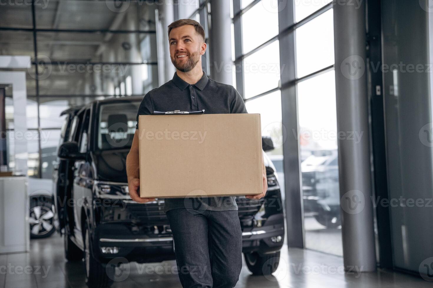 With a ,box,, smiling. Delivery man or loader is near the car photo