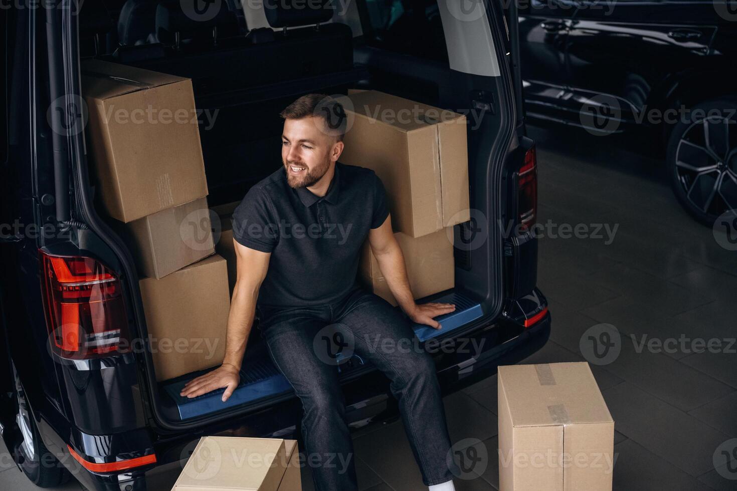 Taking ,a break, resting, sitting. Delivery man or loader is near the car with a box photo