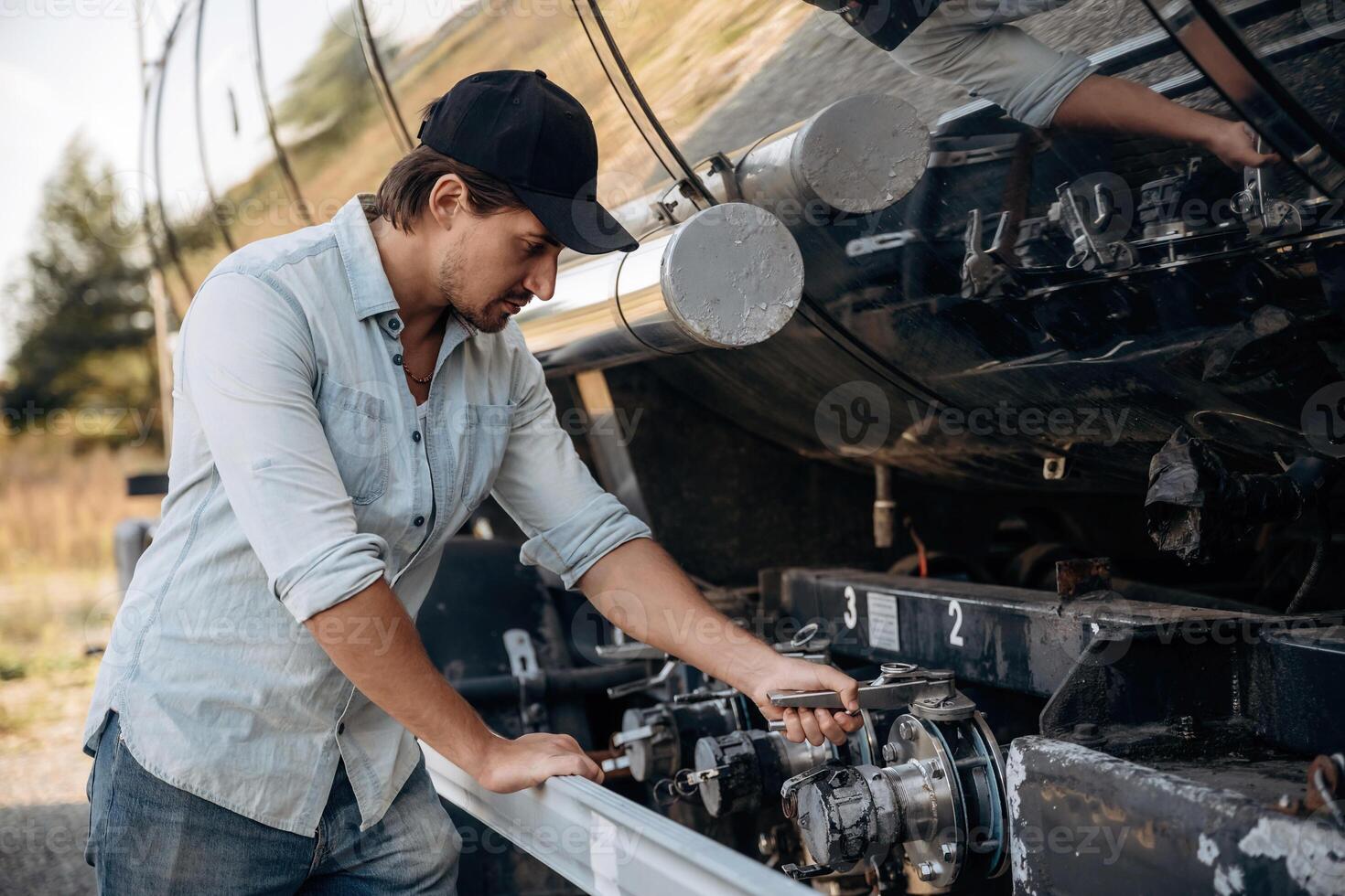 In, shirt ,and in a, cap. Truck driver is near the transport outdoors photo