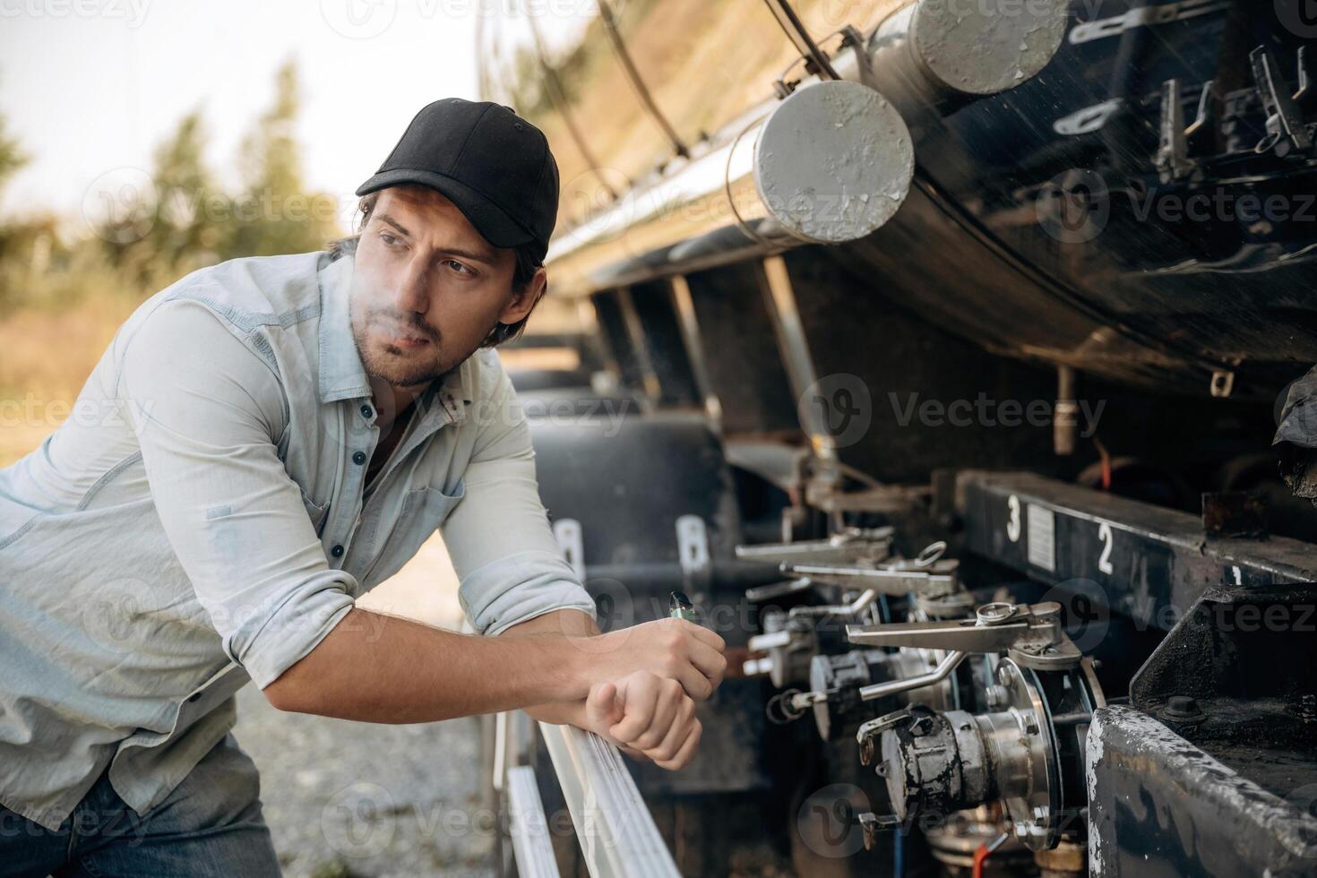 In, shirt ,and in a cap. Truck driver is near the transport outdoors photo