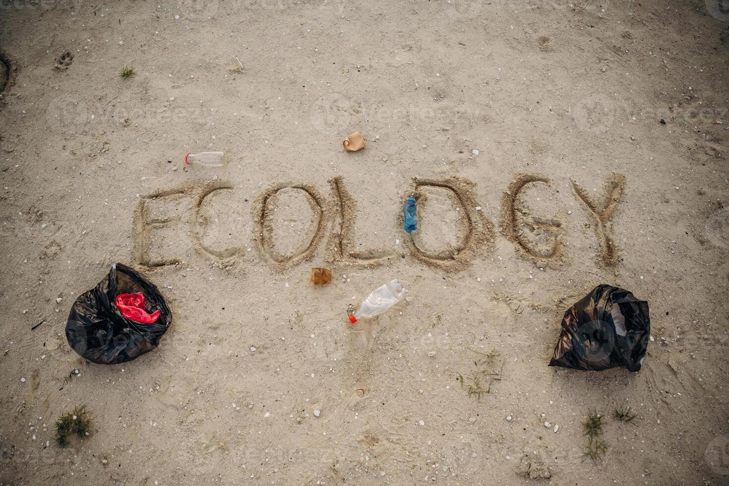 Ecology word written on sand. Plastic bottle, trash bags on the ground. Conception of ecology photo