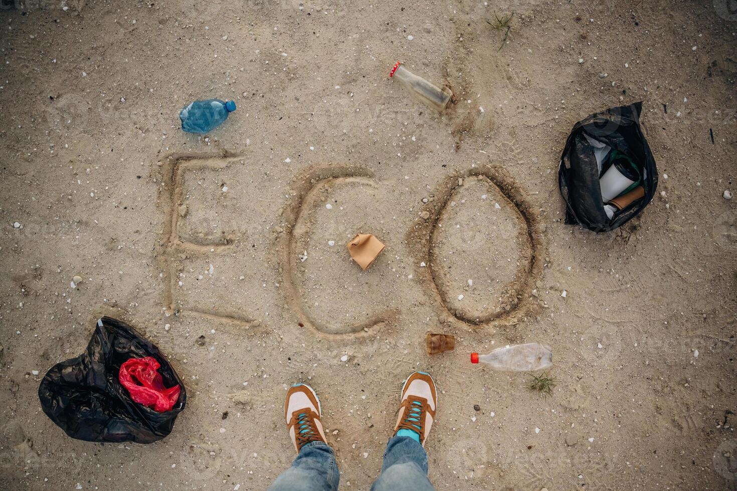 Top view of sand with word eco, trash on the ground, legs of the person photo