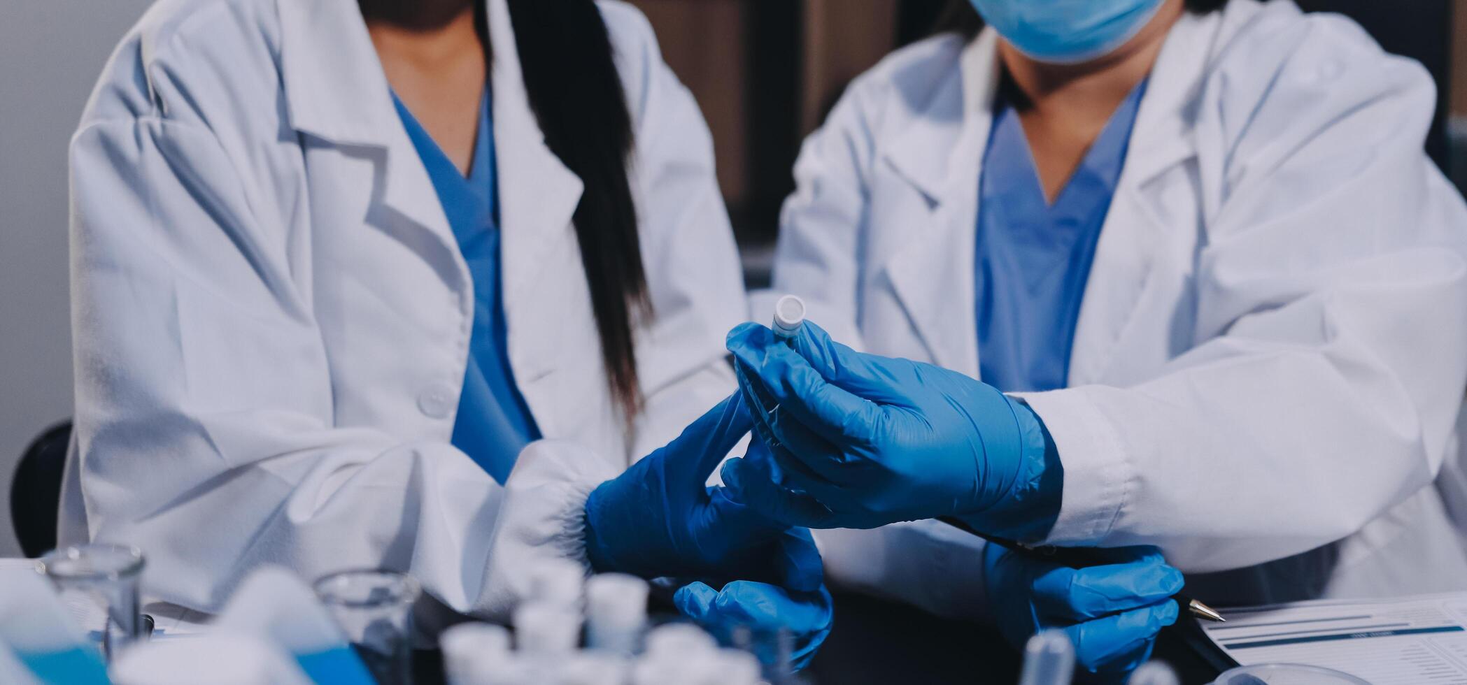 Two women in lab coats and gloves are holding a vial photo
