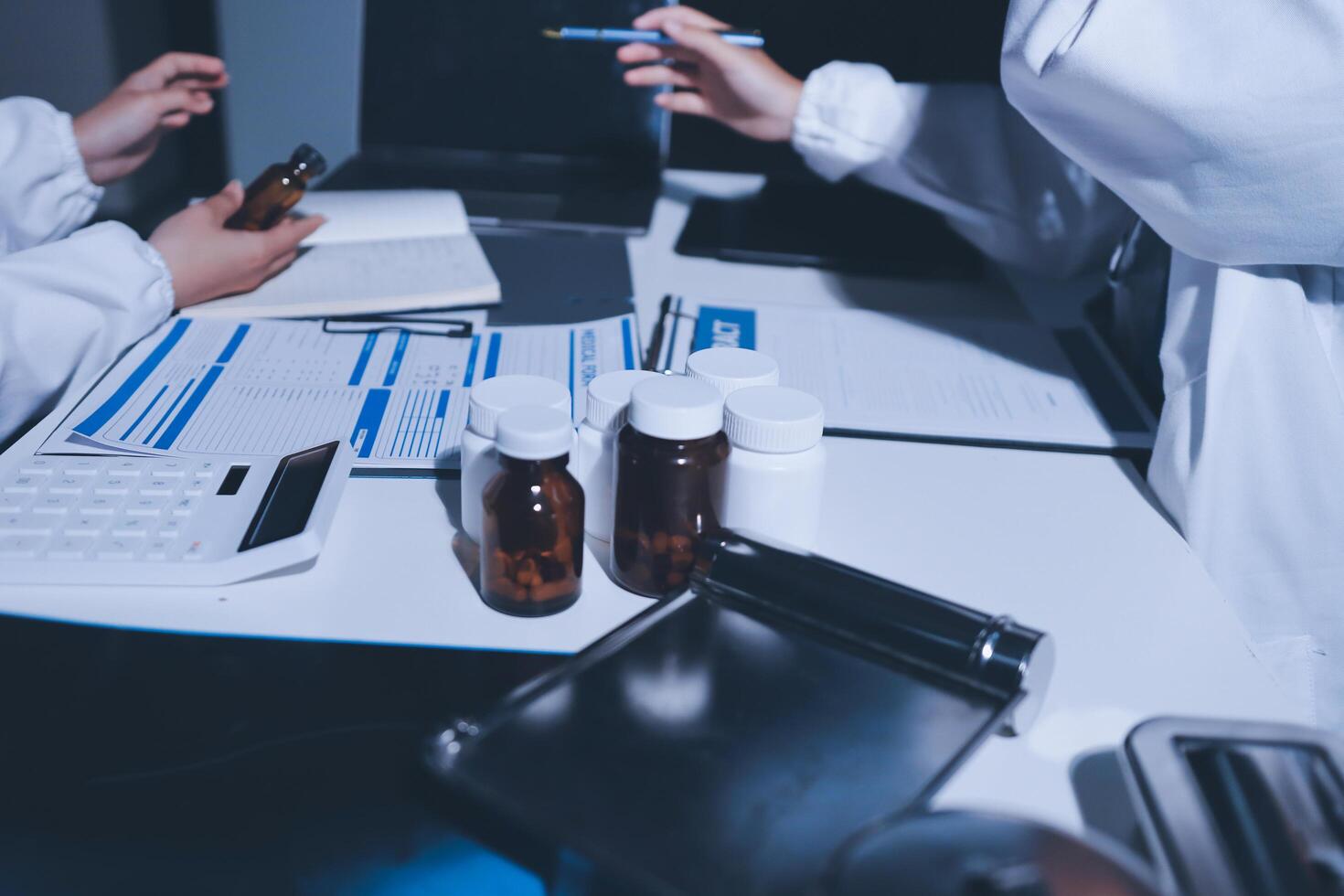 Two people in lab coats sitting at a desk with bottles and other items photo