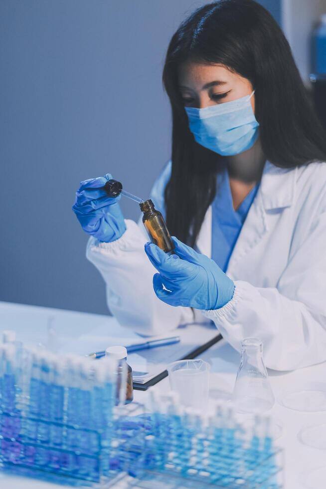A woman in a lab coat and gloves is holding a vial photo